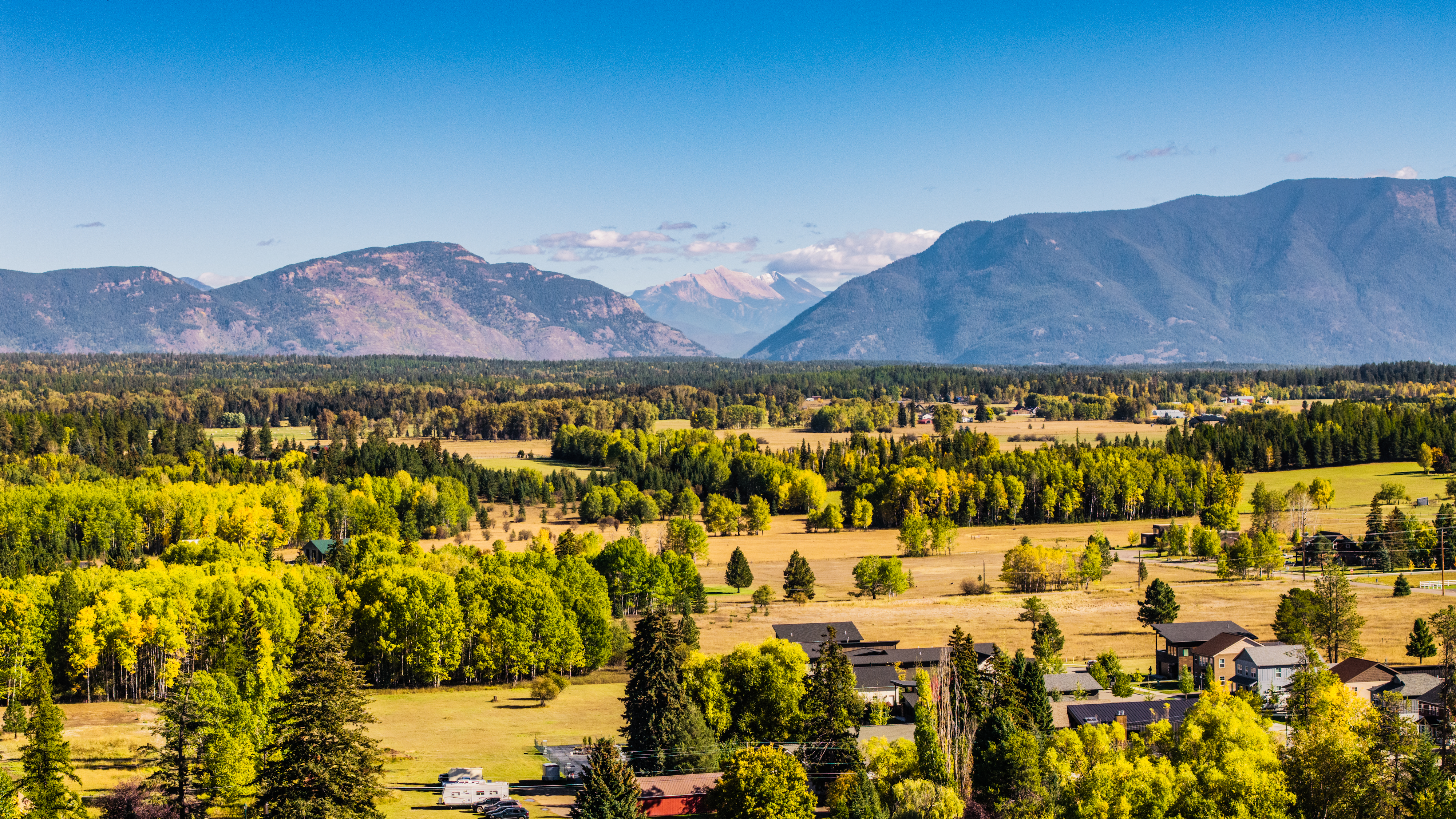 Autumn trees, open fields, and homes beneath the mountains of the Flathead Valley